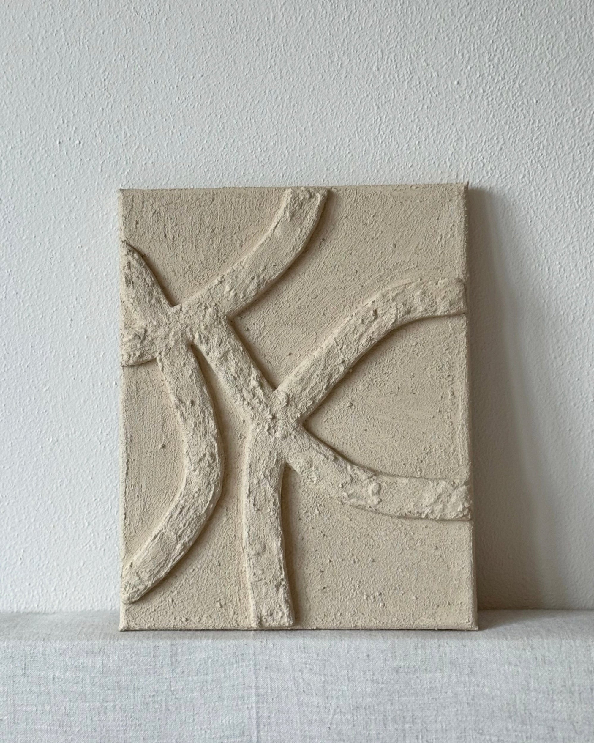 Abstract reliëf kunstwerk in beige met zachte organische lijnen en gelaagde, voelbare structuur aan de muur.