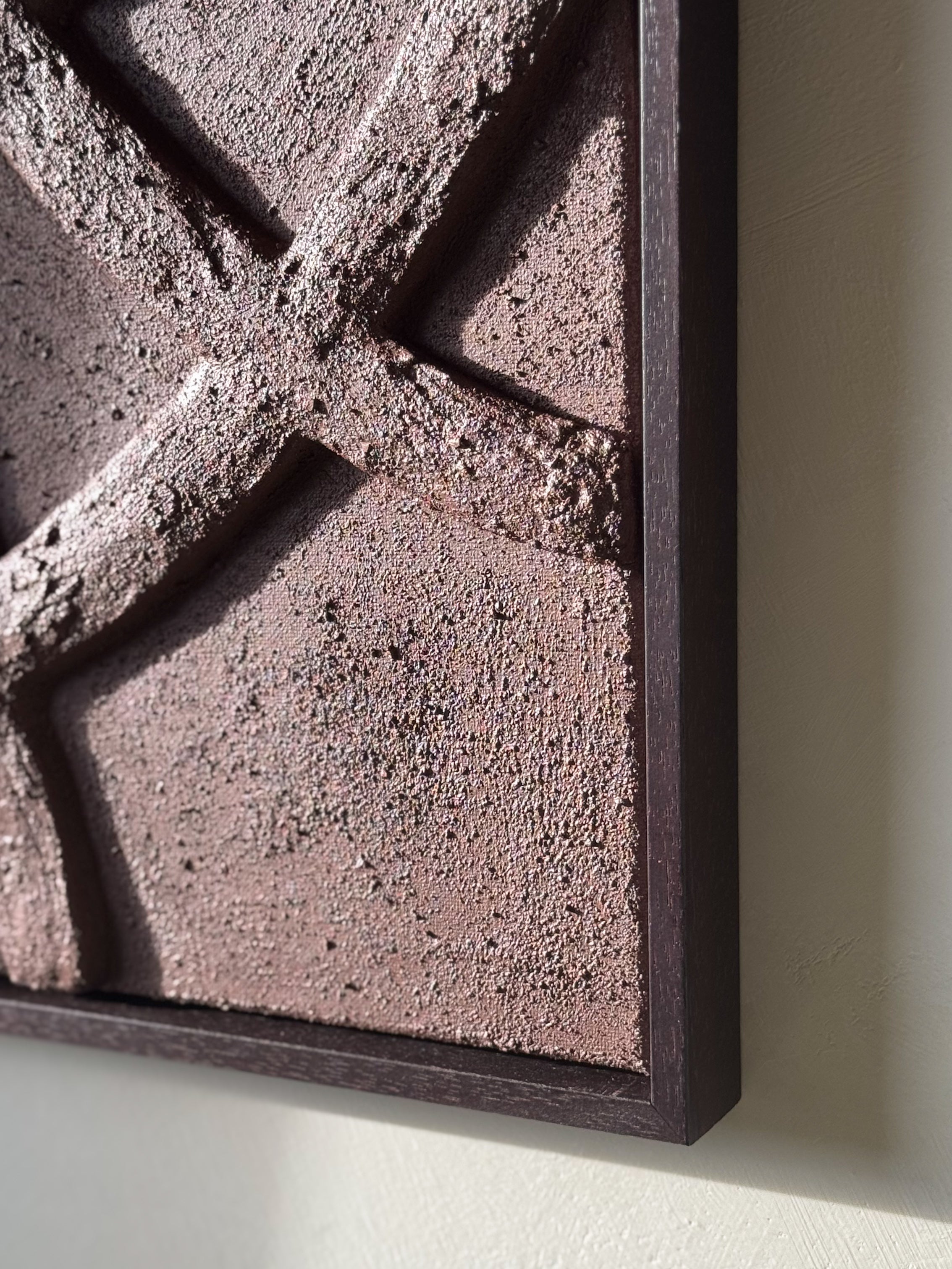 Detail van abstract reliëf wandkunst in chocoladebruin aan de muur in een rustig interieur, met houten lijst en organische vormen, handgemaakt door Studio Lamain.
