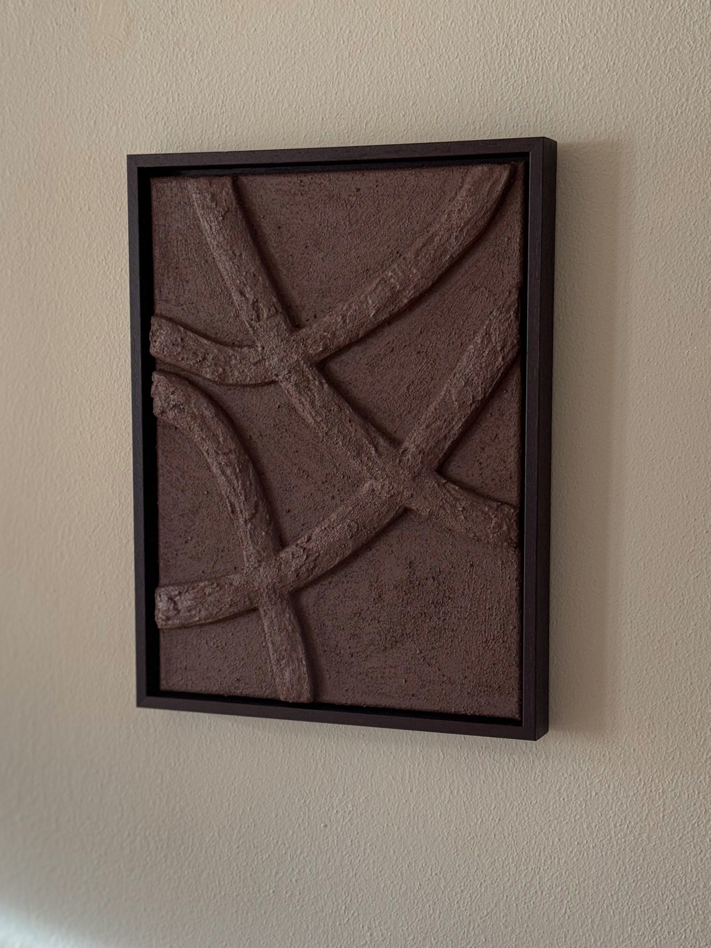Abstract reliëf wandkunst in chocoladebruin aan de muur in een rustig interieur, met houten lijst en organische vormen, handgemaakt door Studio Lamain.