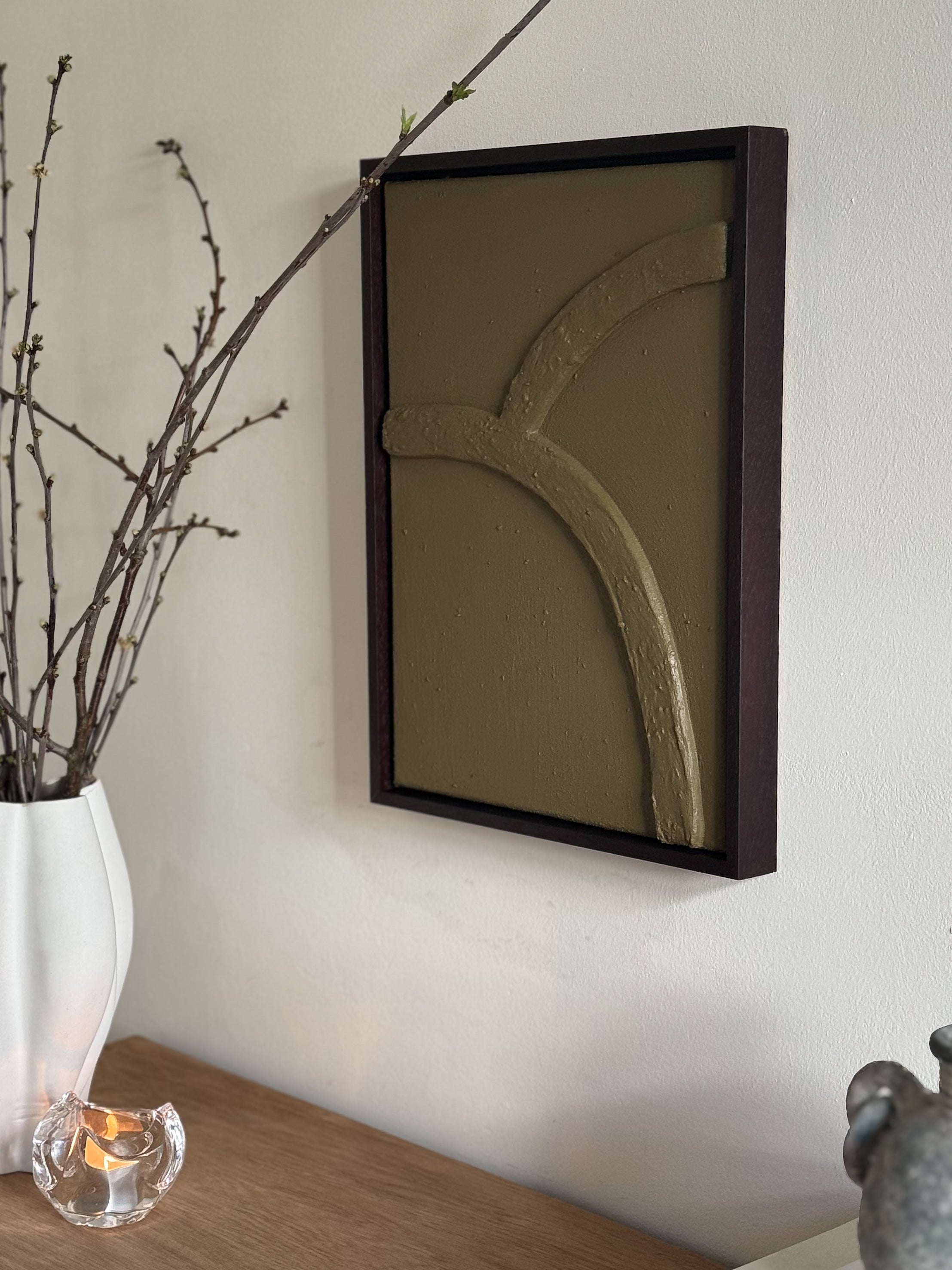 Abstract reliëf wandkunst in olijfgroen met houten lijst aan de muur in Japandi en wabi-sabi interieur, met organische vorm en natuurlijke textuur, handgemaakt door Studio Lamain.