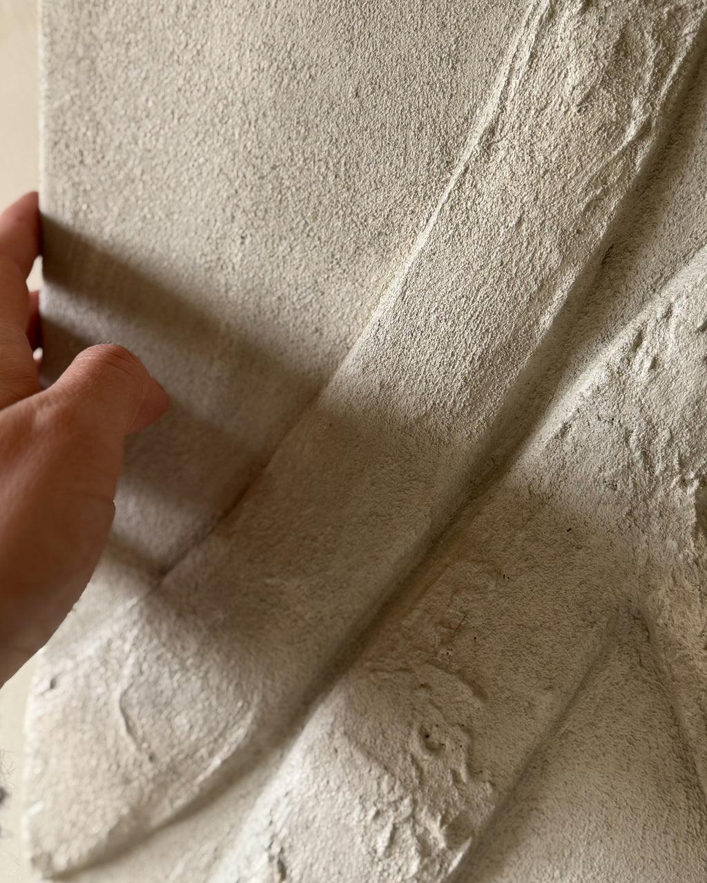 Hand met detail van de textuur van een handgemaakt reliëf kunstwerk met organische lijnen en structuur.