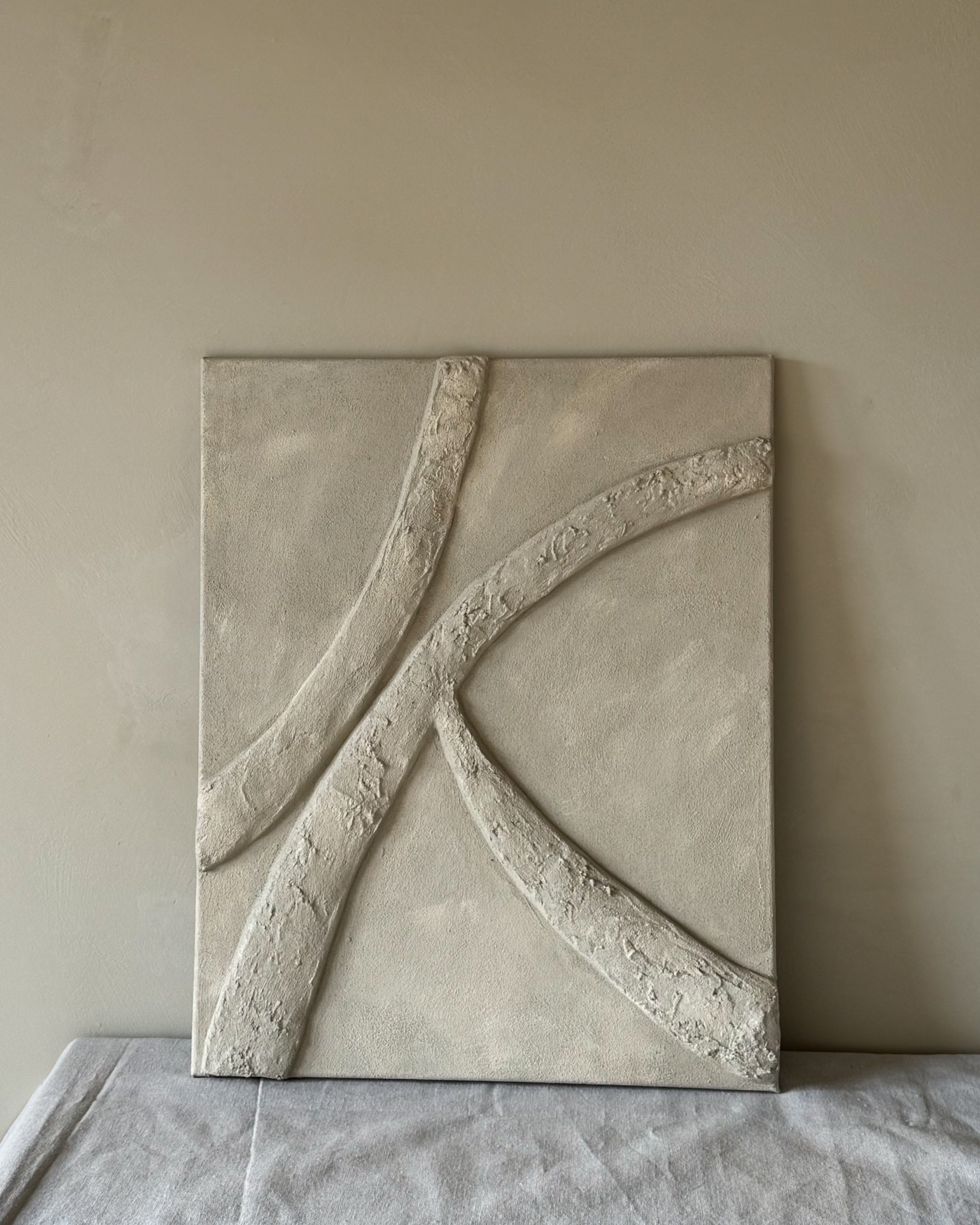 Zandkleurig abstract reliëfkunstwerk met organische lijn aan de muur in een kalm, modern interieur.