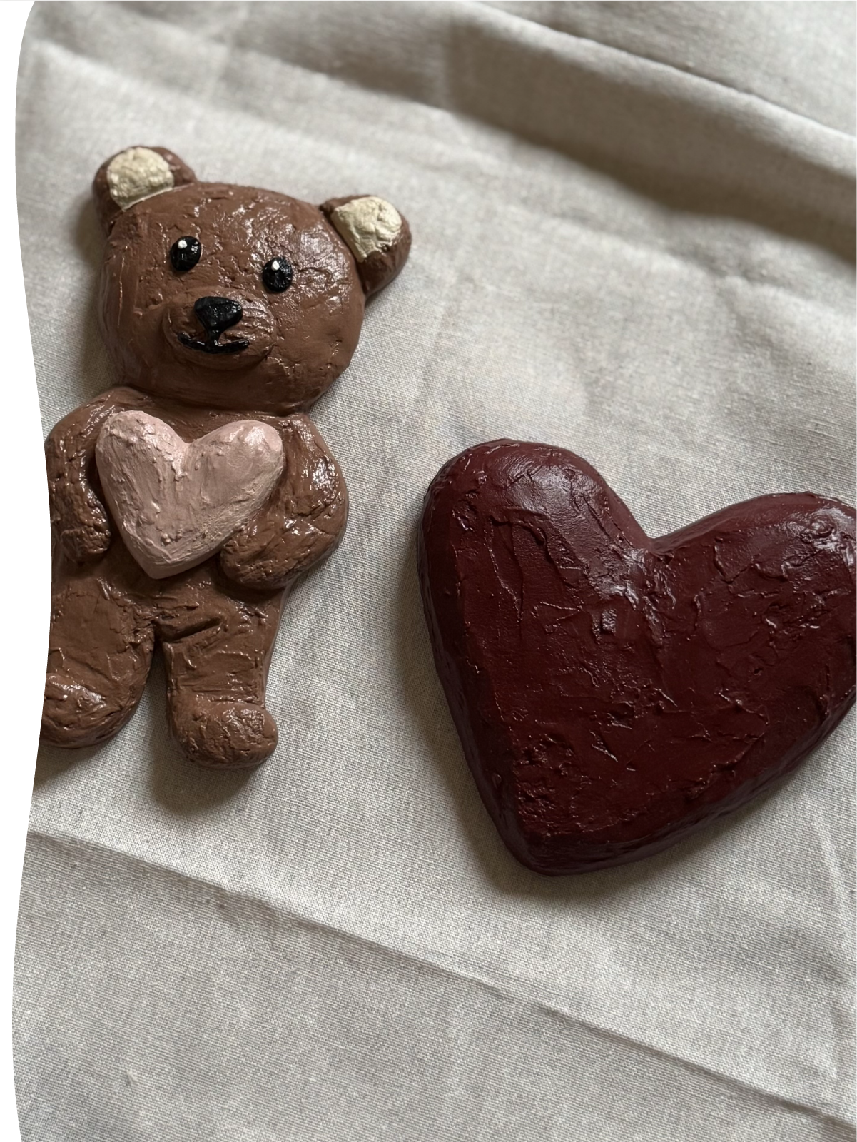 Twee driedimensionale wandobjecten van de Studio Lamain LOve U serie op een linnen doek: een For Always hart in bordeaux en een For Always Bear beer met nude kleurig hart voor op de kinderkamer.