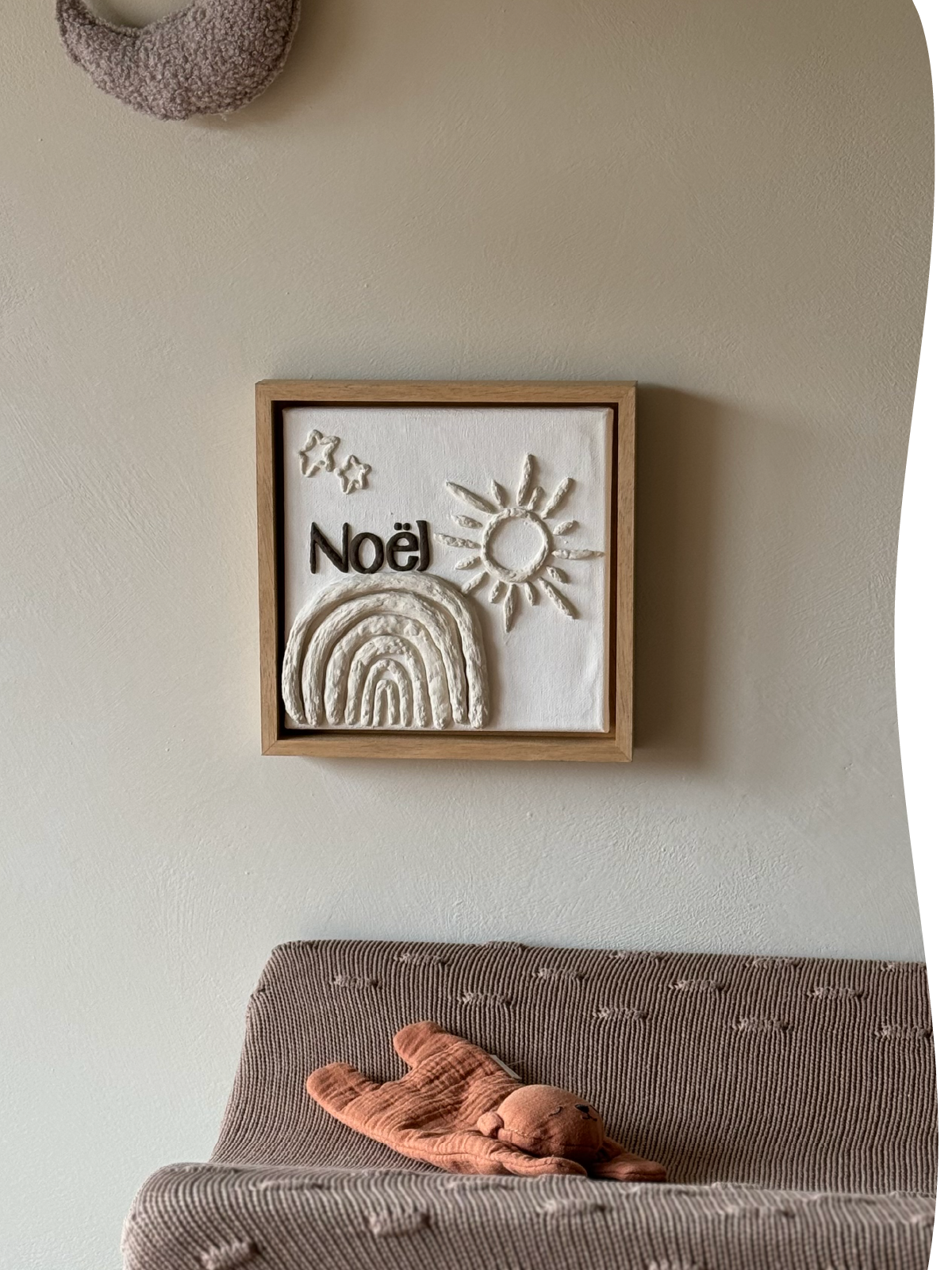 Een geboortekaartje op canvas in reliëf, gebaseerd op het geboortekaartje van Noël met zon, regenboog en sterren in zachte kleuren op een kinderkamer.