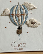 Detail van handgemaakt reliëfkunstwerk voor Chez met luchtballon, wolken en vogel in zachte tinten, gebaseerd op zijn geboortekaartje.