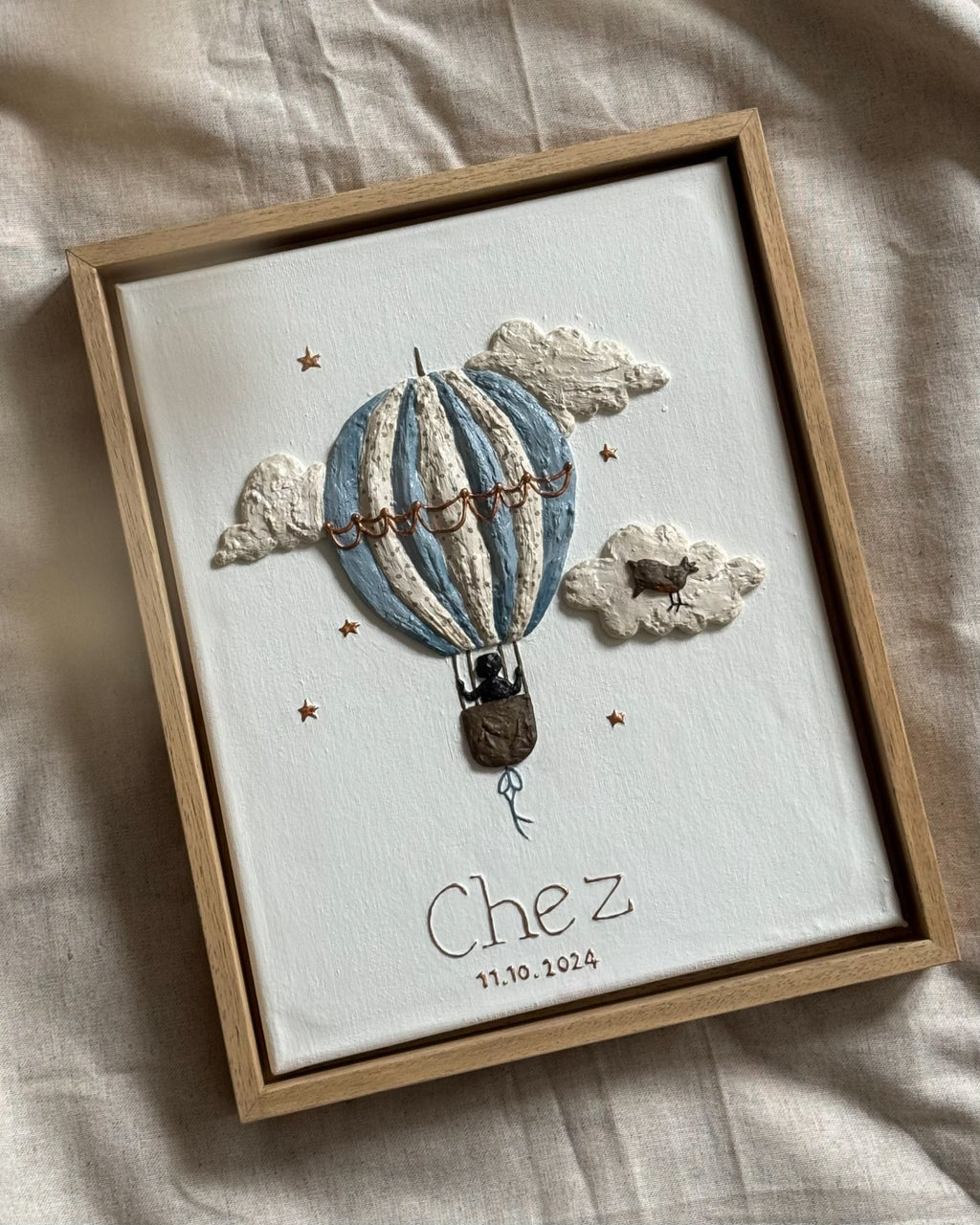 Geboortekaartje van Chez vertaald naar handgemaakt reliëfkunstwerk met luchtballon, wolken en vogel in zachte tinten.