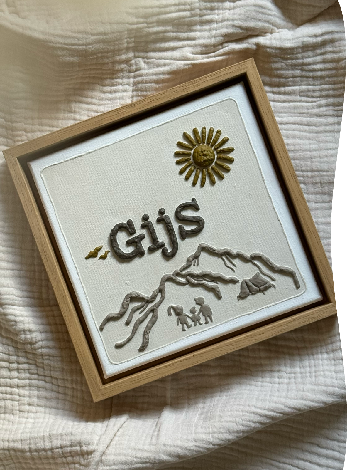 Een reliëfkunstwerk van het geboortekaartje van Gijs met naam, zon, bergen en kamperend gezin op een doek.