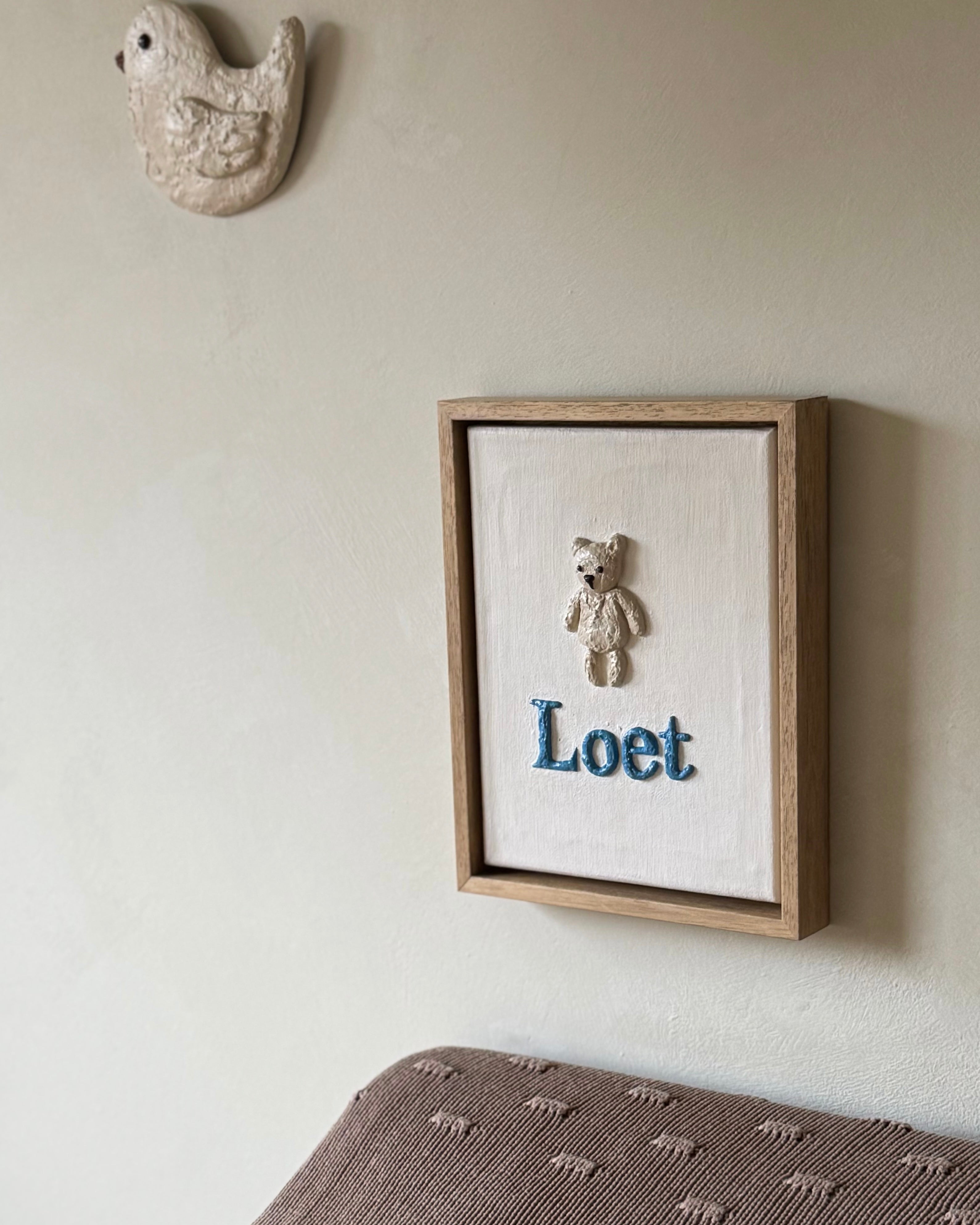 Reliëfkunstwerk gebaseerd op het geboortekaartje van Loet in zachte aardetinten aan de muur op kinderkamer.