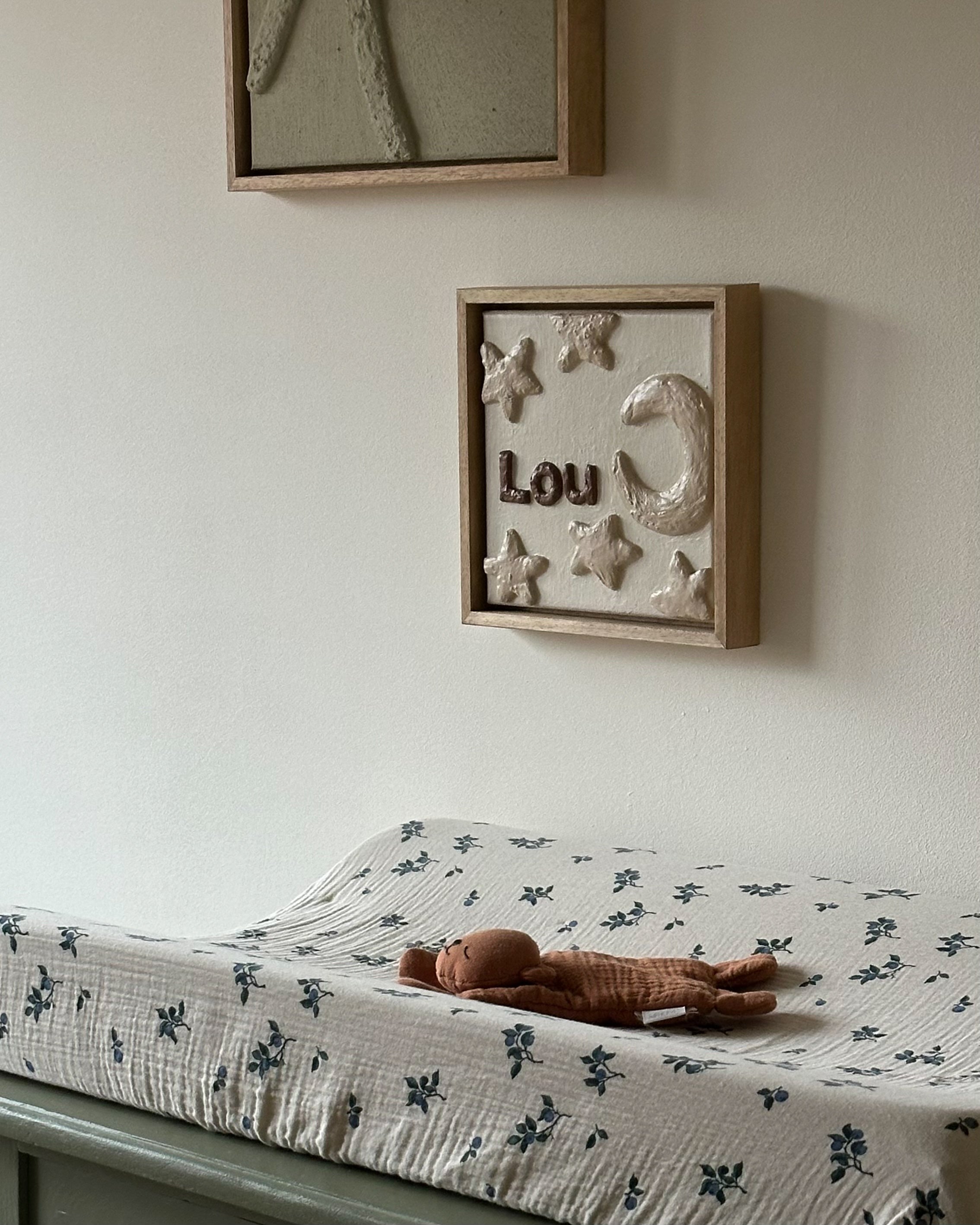 Handgemaakt reliëfkunstwerk voor Lou, gebaseerd op zijn geboortekaartje met sterren de de maan in aardetinten aan de muur op een kinderkamer.