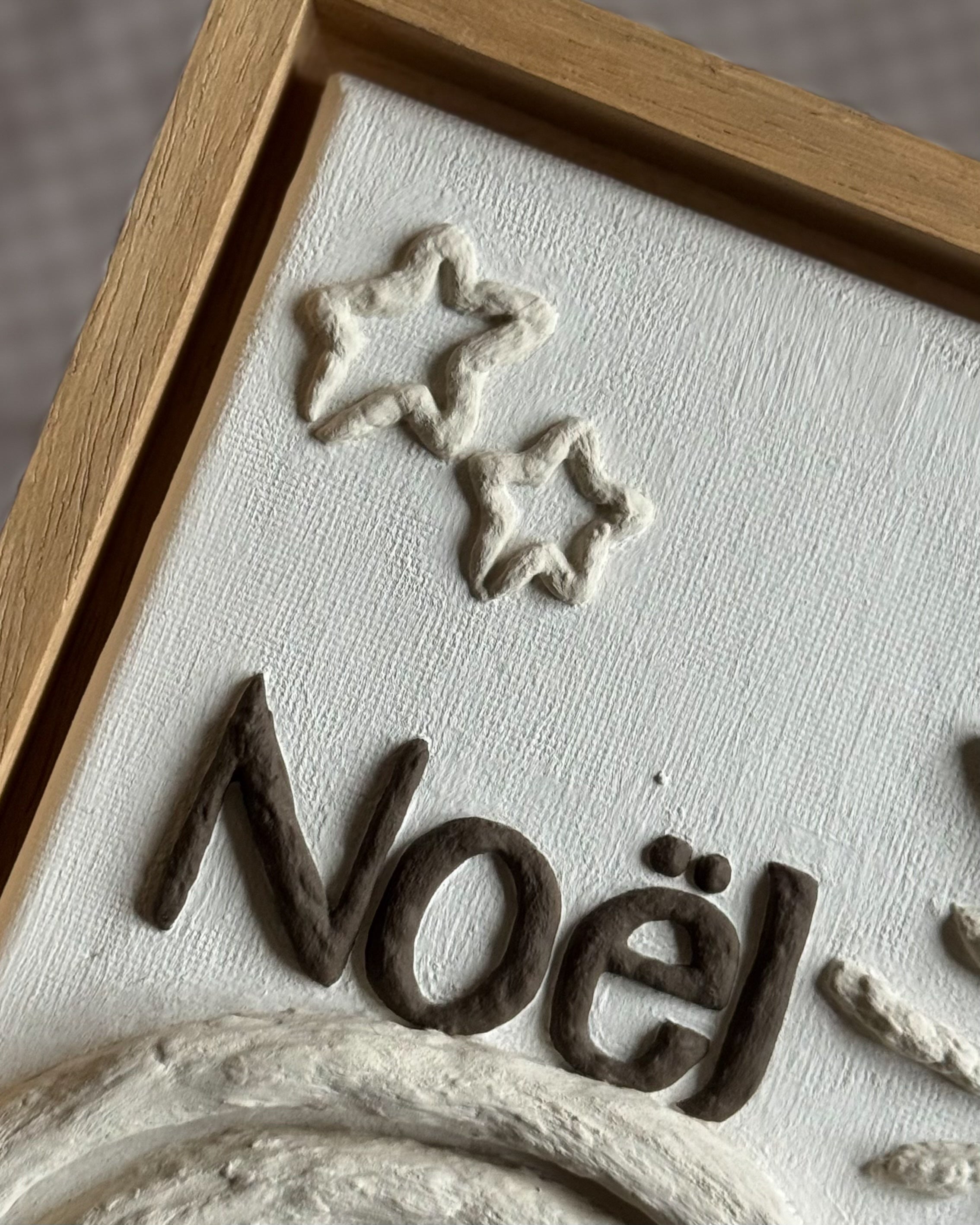 Detail van handgemaakt reliëfkunstwerk voor Noël, gebaseerd op zijn geboortekaartje in zachte tinten met handgemaakte lijst.
