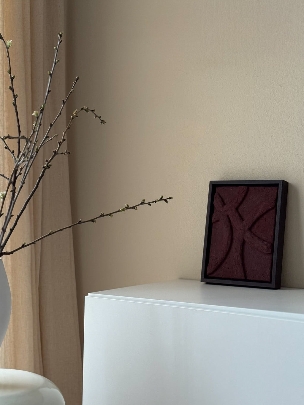 Het bordeauxrode handgemaakte 3D kunstwerk in noten houten lijst van Studio Lamain in een rustig beige interieur.